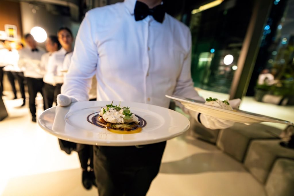 Server presenting a plated course at the AGMC × Lotus private dinner